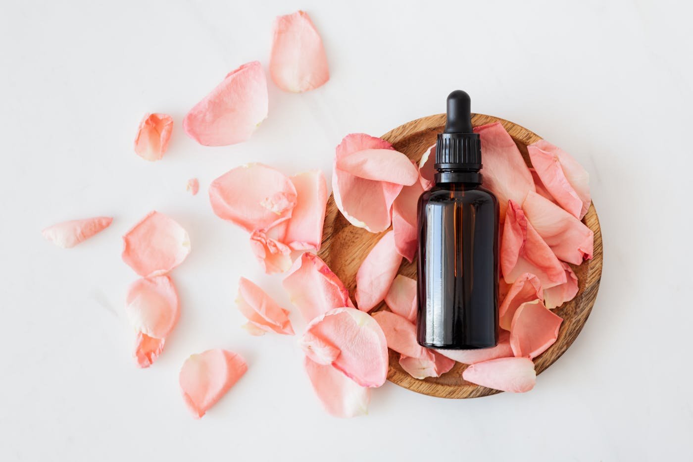 Contagocce in vetro ambrato su un piattino di legno circondato da petali di rosa